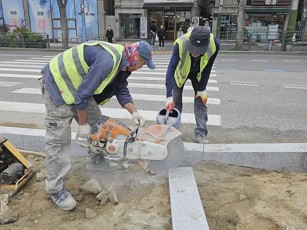 안전조끼를 입은 작업자 두 명이 절단기로 경계석을 자르는 현장